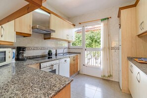 A kitchen with granite countertops, a stove, a microwave, and wooden cabinets. - Villa Encina by Villa Plus (Teulada)
