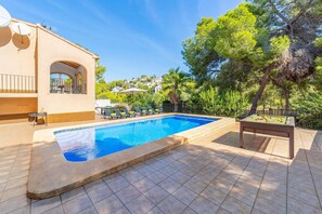 A swimming pool with lounge chairs and a pool table, surrounded by trees and a building with a balcony. - Villa Encina by Villa Plus (Teulada)