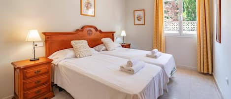 A double bed with a wooden headboard, two bedside tables, and a window with curtains.