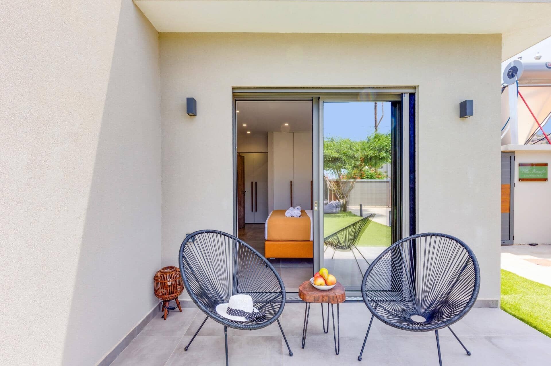 Een balkon met twee zwarte draadstoelen, een klein houten tafeltje met een schaal fruit, en een rieten stoel.