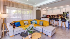 A modern living room with a sofa, coffee table, and a kitchen area with bar stools. - Villa Manefic by Villa Plus (Malevizi)