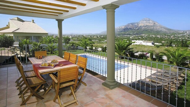 A terrace with a pool, wooden furniture, and a mountain view. - Villa Tia Elanor by Villa Plus (Jávea)