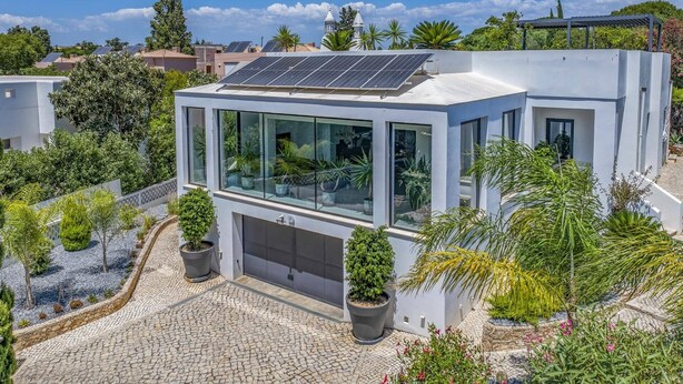 A modern house with a solar panel roof, a garage, and a garden with various plants.