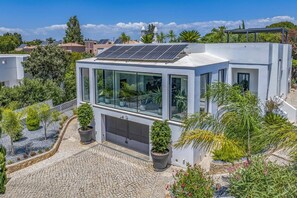 A modern house with a solar panel roof, a garage, and a garden with various plants. - Villa Sylisia by Villa Plus (Praia do Carvoeiro)