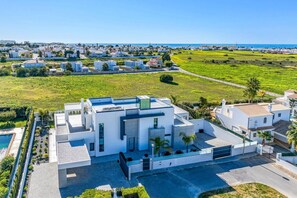 A modern building with a flat roof, surrounded by a well-maintained lawn and a clear view of the sea. - Villa Opala by Villa Plus (Vale Rebelho)