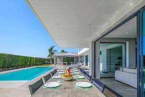 A modern outdoor dining area with a pool, dining tables set with plates and glasses, and a view of the pool and greenery. - Villa Opala by Villa Plus (Vale Rebelho)