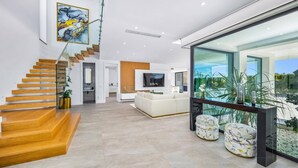 Ein modernes Wohnzimmer mit Treppe, einem Flachbildfernseher und einem großen Fenster mit Blick auf einen Garten.