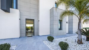 Ein modernes Gebäude mit flacher Fassade, einem Glastürbereich und einem befestigten Weg mit weißen Kieselsteinen und kleinen Büschen.