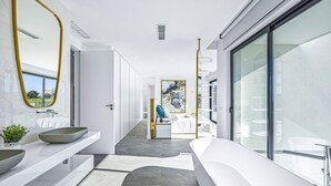 Ein modernes Badezimmer mit einer großen Badewanne, einem runden Waschbecken und einem Spiegel mit goldener Rahmung.