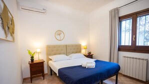 A bedroom with a bed, bedside tables, a radiator, and a window with curtains.