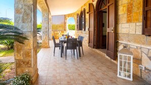 A covered patio with stone walls, arched windows, and a table with chairs.