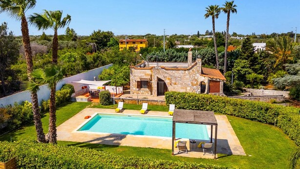 A villa with a swimming pool, surrounded by lush greenery and palm trees.