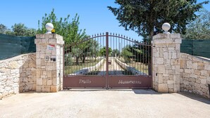 Una entrada cerrada con muros de piedra y una reja metálica, que conduce a un camino.
