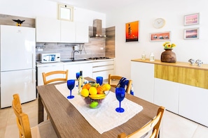 Una cocina moderna con armarios blancos, horno empotrado y comedor con mesa y sillas de madera.