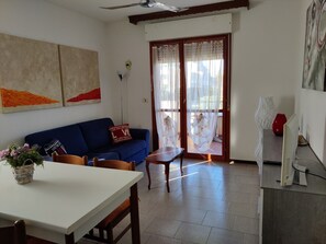 Un salon comprenant un canapé, une table à manger et un téléviseur. Il y a une porte-fenêtre coulissante avec des rideaux.