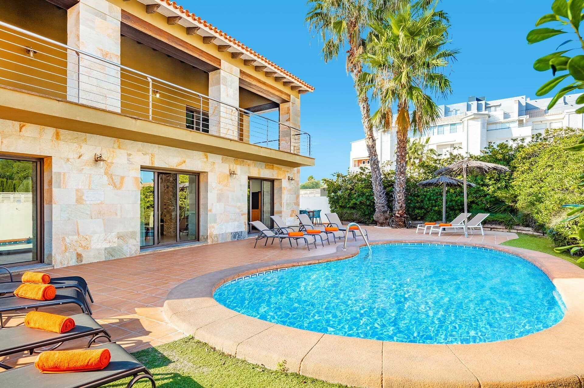 A modern building with a swimming pool, lounge chairs, and palm trees.
