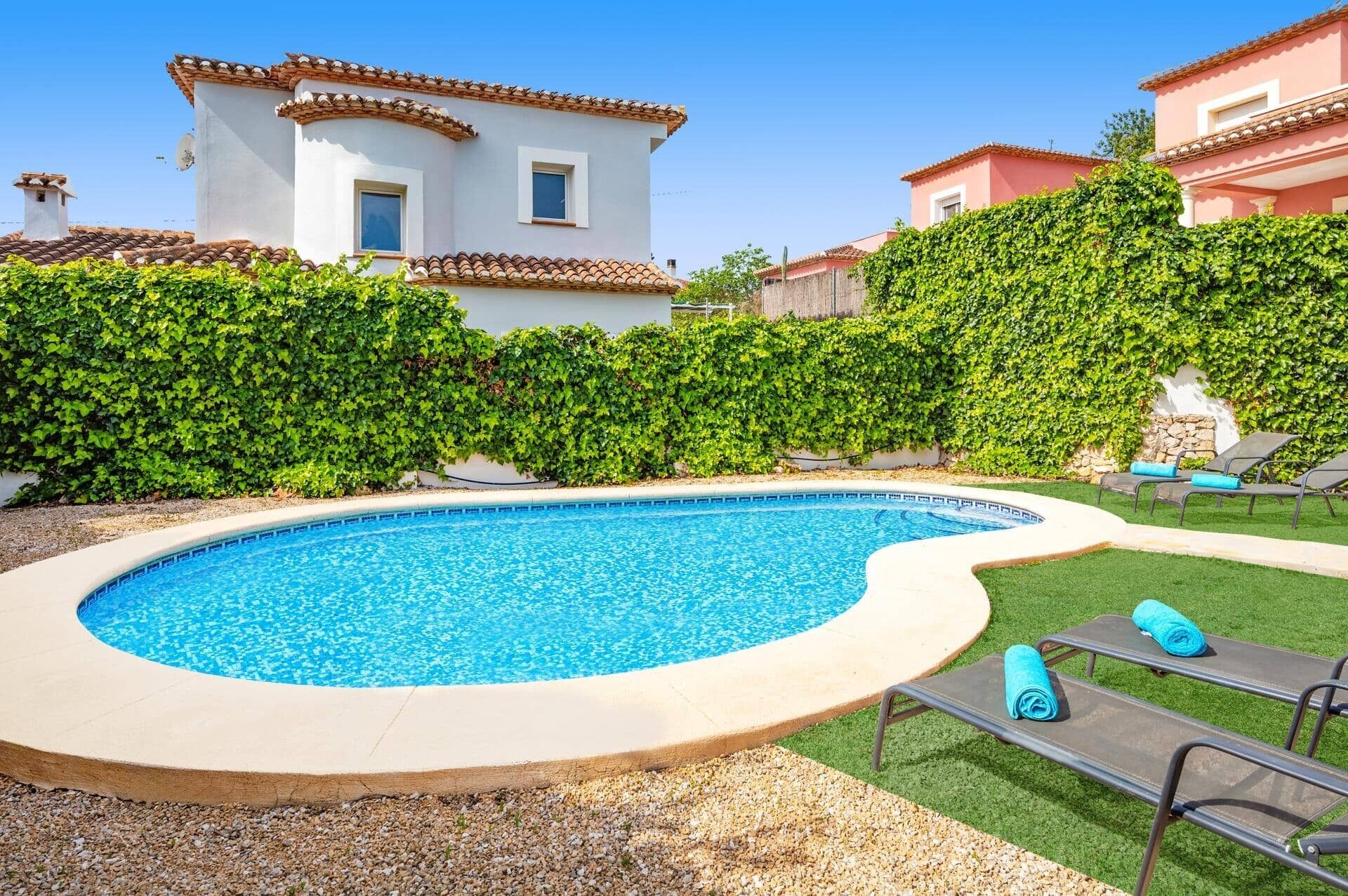 Una piscina con hidromasaje, rodeada por un seto y una zona verde con sillones de descanso.