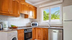 A kitchen with wooden cabinets, a microwave, oven, dishwasher, and a washing machine. - Villa Jazmin Blanca by Villa Plus (Beniarbeig)