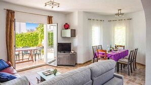 A living room with a sofa, a TV, and a dining area with a table set for two. - Villa Jazmin Blanca by Villa Plus (Beniarbeig)