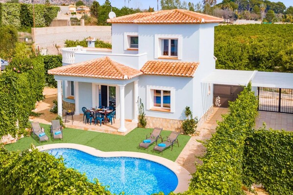 A two-story house with a swimming pool, outdoor seating, and a garden.