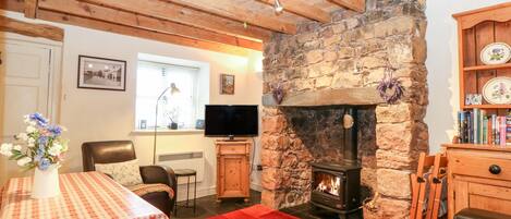 A cozy living room with a stone fireplace, wooden beams, a television, and a dining area with a checkered tablecloth.