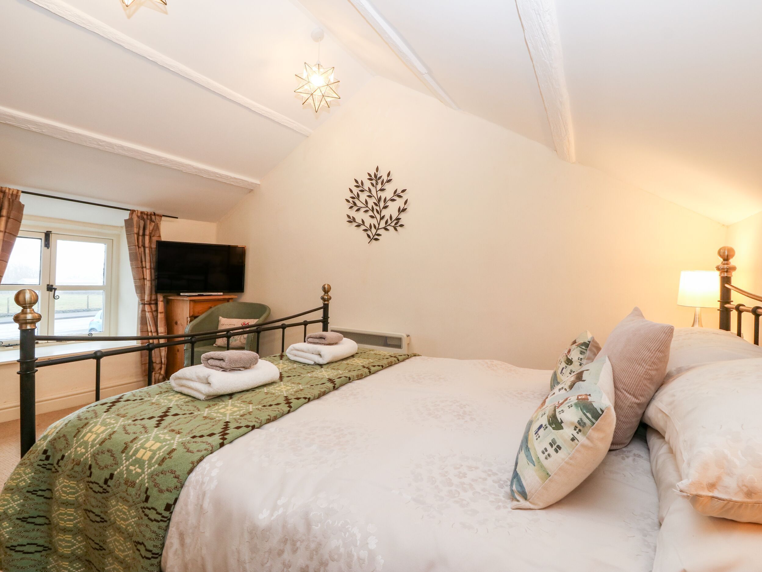Een net opgemaakt bed met handdoeken, een televisie aan de muur en een raam met gordijnen.
