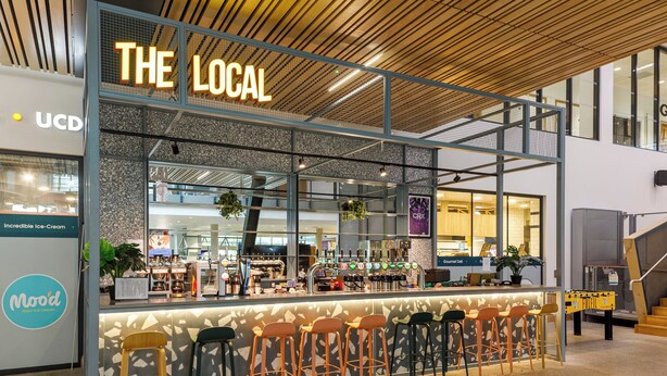 A café named "The Local" with a modern design, featuring a bar area with stools and a variety of seating options. - UCD Campus Accommodation (Dublin)