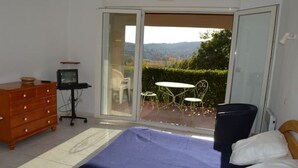 Une chambre à coucher avec un lit, une commode, un bureau avec un ordinateur et une vue sur l’extérieur.