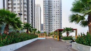 Un paseo marítimo de madera con jardineras y palmeras, que conduce a una zona de estar cubierta.