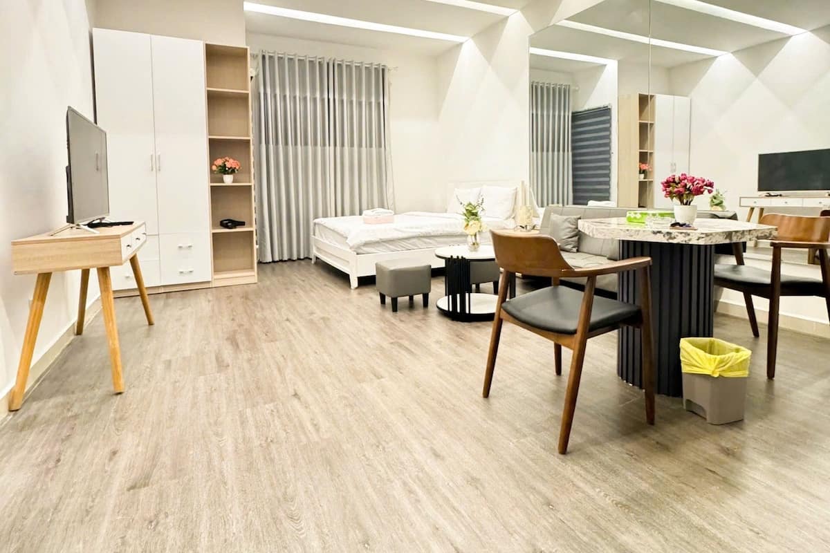 Ein modernes Schlafzimmer mit einem Bett, Nachttischen, einem Schreibtisch und einem Sessel. Links befindet sich ein Kleiderschrank und ein Fernseher.