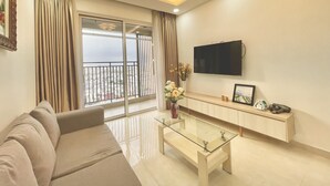 Una sala moderna con sofá, una mesa de centro de vidrio, televisor montado en la pared y balcón con vistas.