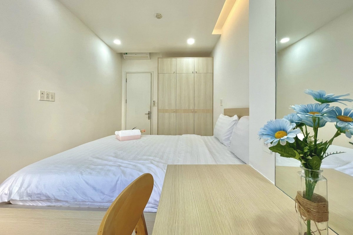 Ein Hotelzimmer mit einem Bett, einem Holztisch, einem Stuhl, einem Spiegel und einer Vase mit Blumen.