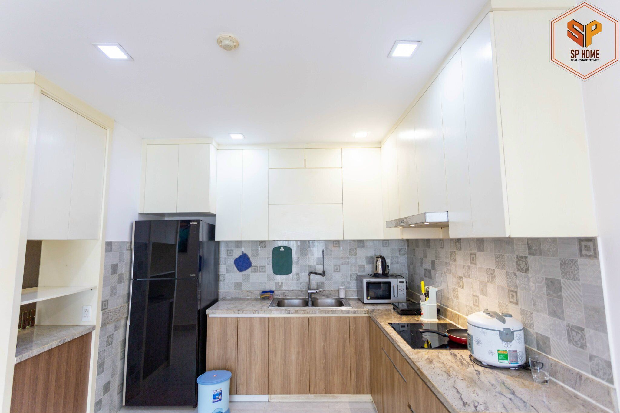 Una cocina moderna con armarios blancos, un refrigerador negro, un microondas y una cocedora de arroz.