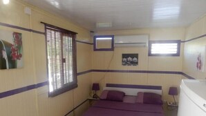 Ein Schlafzimmer mit einem Bett, zwei Nachttischen, einem Fenster mit Jalousien, einer Klimaanlage und einem kleinen Bild an der Wand.