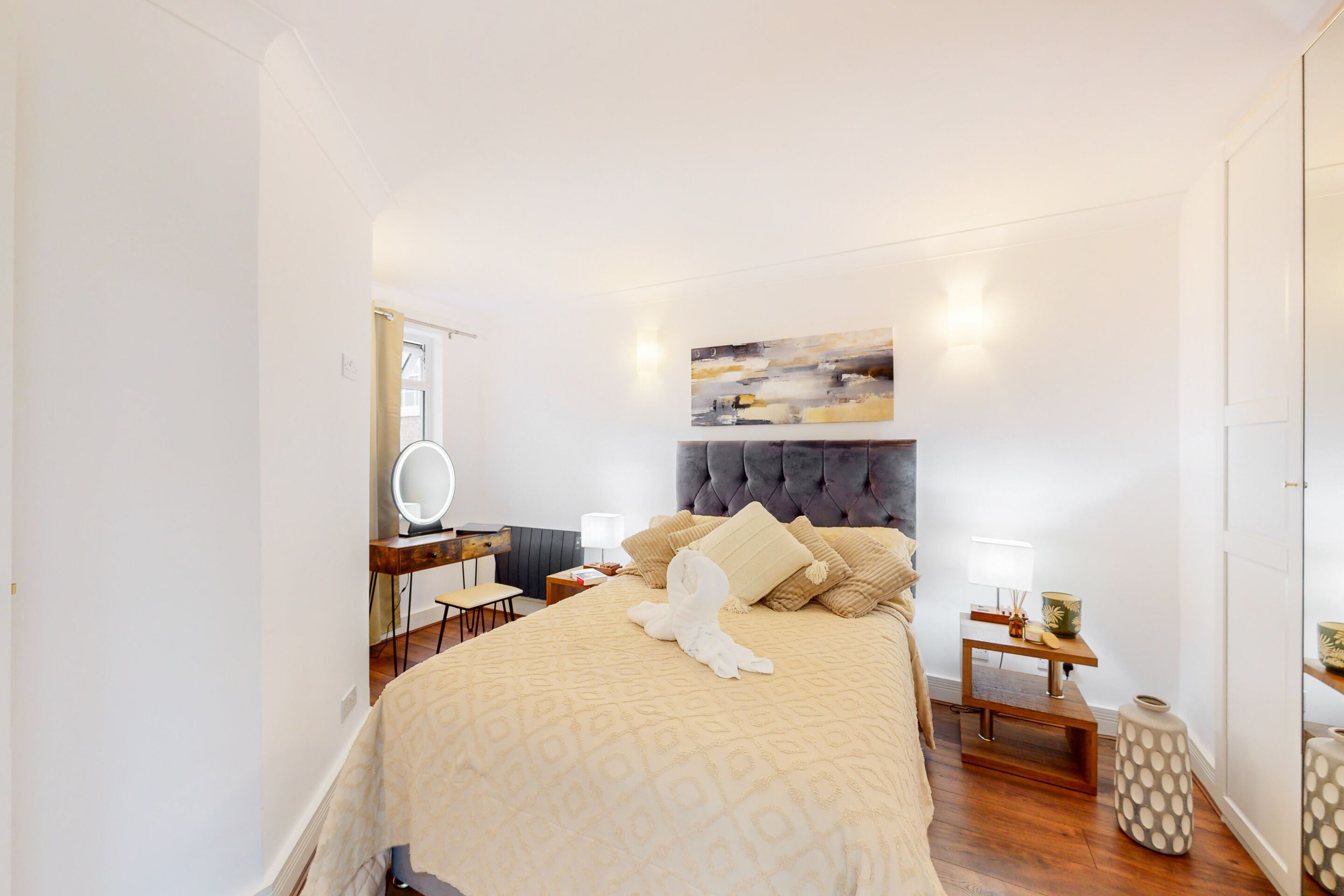 Une chambre à coucher avec un grand lit, une table de chevet avec une lampe, un miroir et une œuvre d’art accrochée au mur.