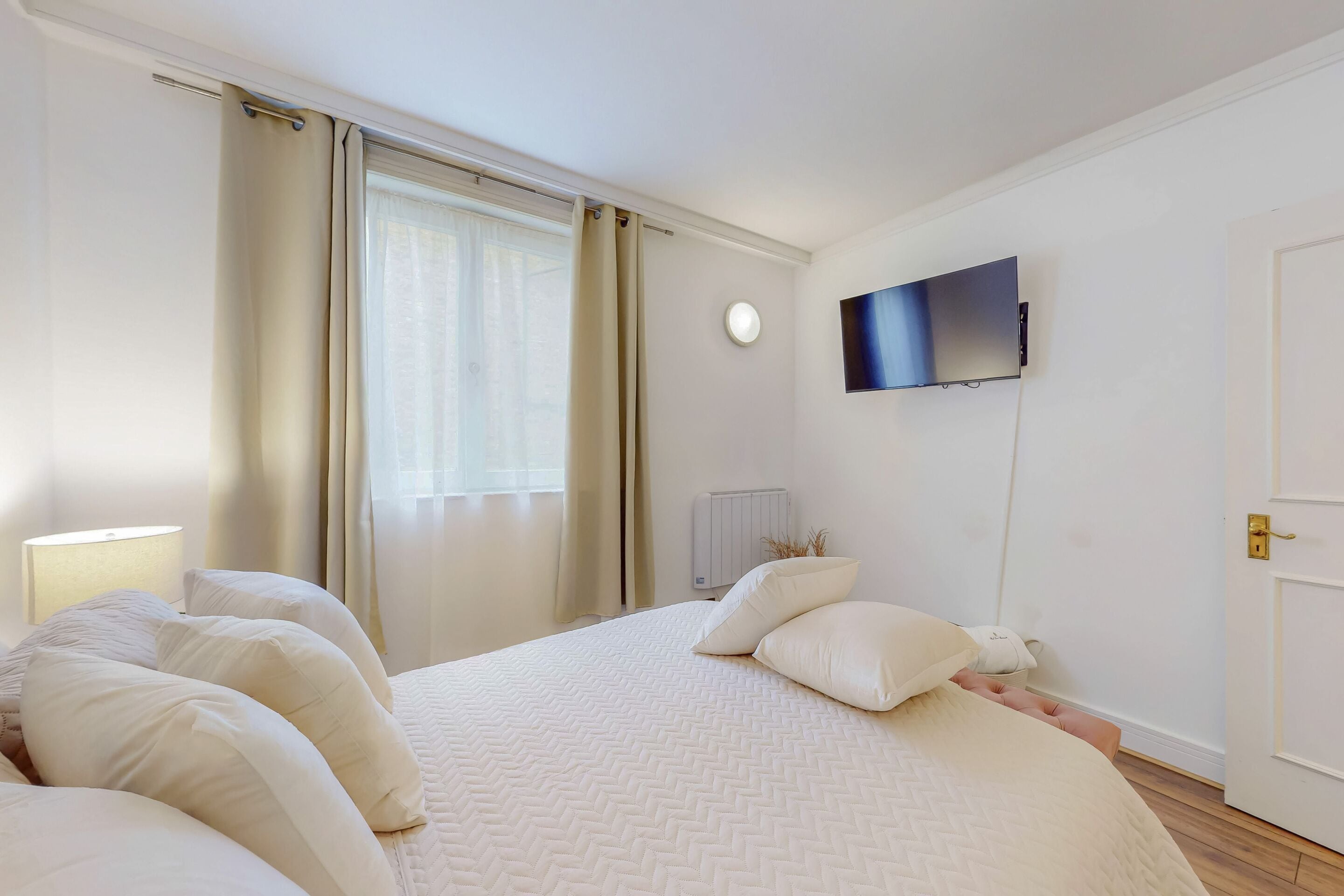 Un dormitorio con una cama grande, un televisor de pantalla plana en la pared, un radiador y una puerta.