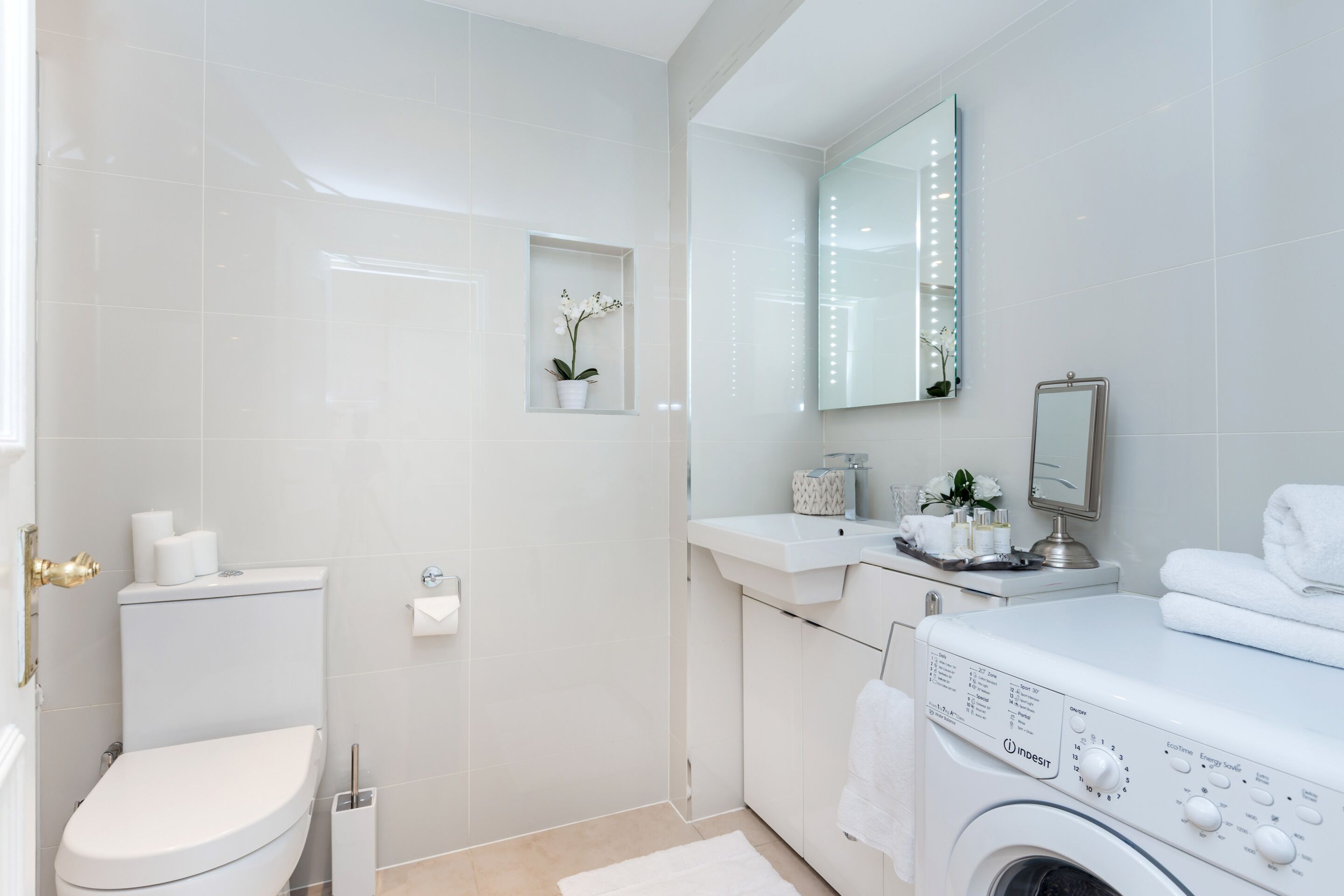 A modern bathroom with a toilet, sink, mirror, and washing machine.