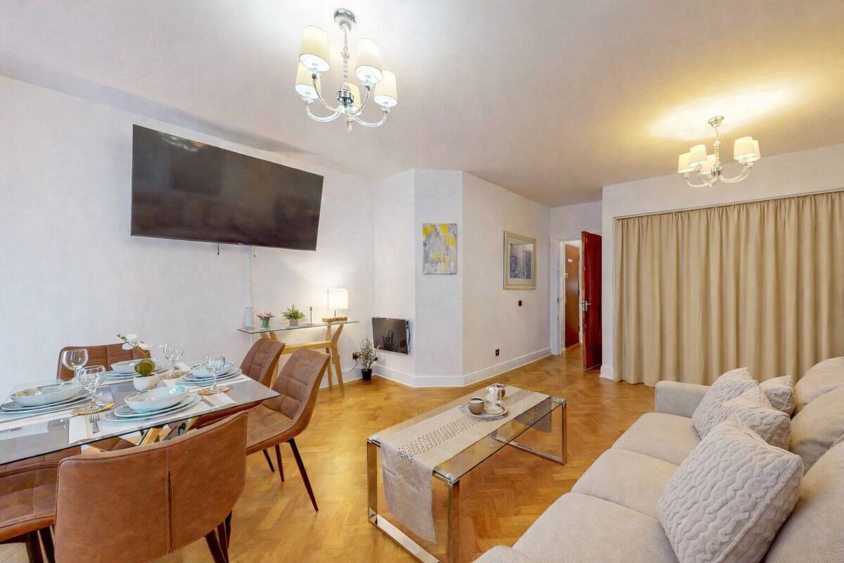A modern living room with a dining area, a flat-screen TV mounted on the wall, and a sofa set.
