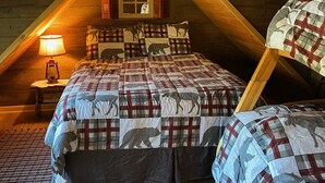 A cozy attic bedroom with a sloped ceiling, a wooden bed with a plaid comforter, a small window with string lights, and a nightstand with a lantern. - Pondside Paradise (Singers Glen)