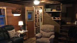 A cozy living room with a leather couch, a beige armchair, and a small table with a lamp. A wooden door leads to a staircase. - Pondside Paradise (Singers Glen)