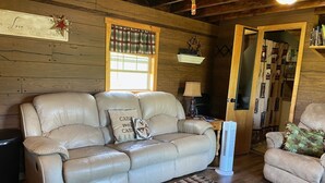 A cozy living room with a leather sofa, a small rug, and a window with plaid curtains. - Pondside Paradise (Singers Glen)