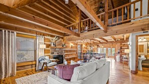 Un intérieur spacieux de chalet en bois, avec un plafond haut, une cheminée, un coin repas et un espace salon confortable.