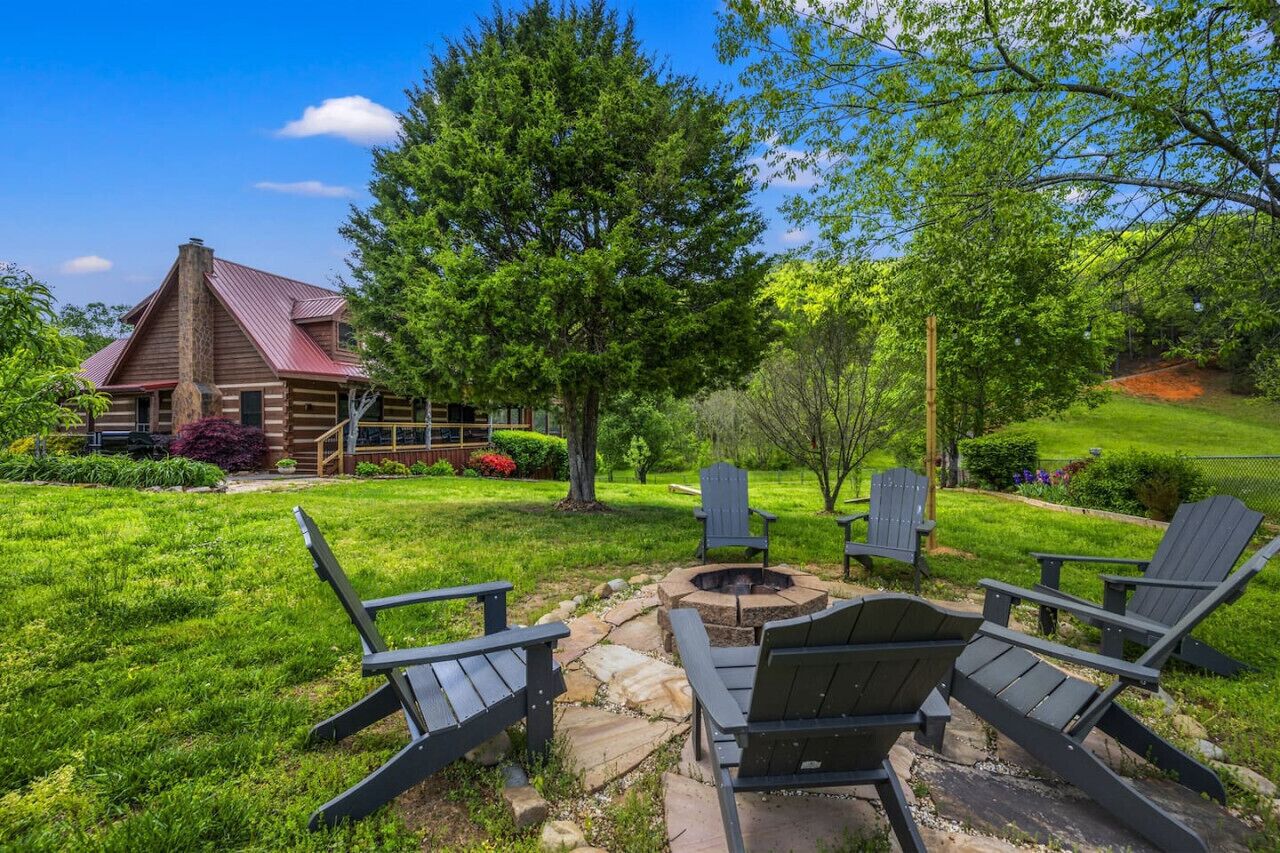 Une cabane en rondins avec un foyer et des fauteuils Adirondack, le tout situé dans un jardin luxuriant.