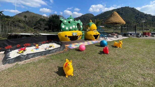 A grassy area with colorful play structures and a thatched-roof pavilion. - mijingminsu (Yuchi)