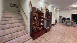 A hotel lobby with a staircase, a wooden display cabinet with various items, a television, and seating area. - mijingminsu (Yuchi)