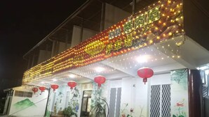 A building with a brightly lit sign, outdoor seating, and decorative plants. - mijingminsu (Yuchi)
