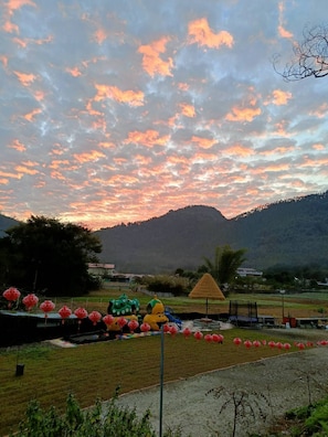 A park with playground equipment, a thatched-roof structure, and a view of a mountain range. - mijingminsu (Yuchi)