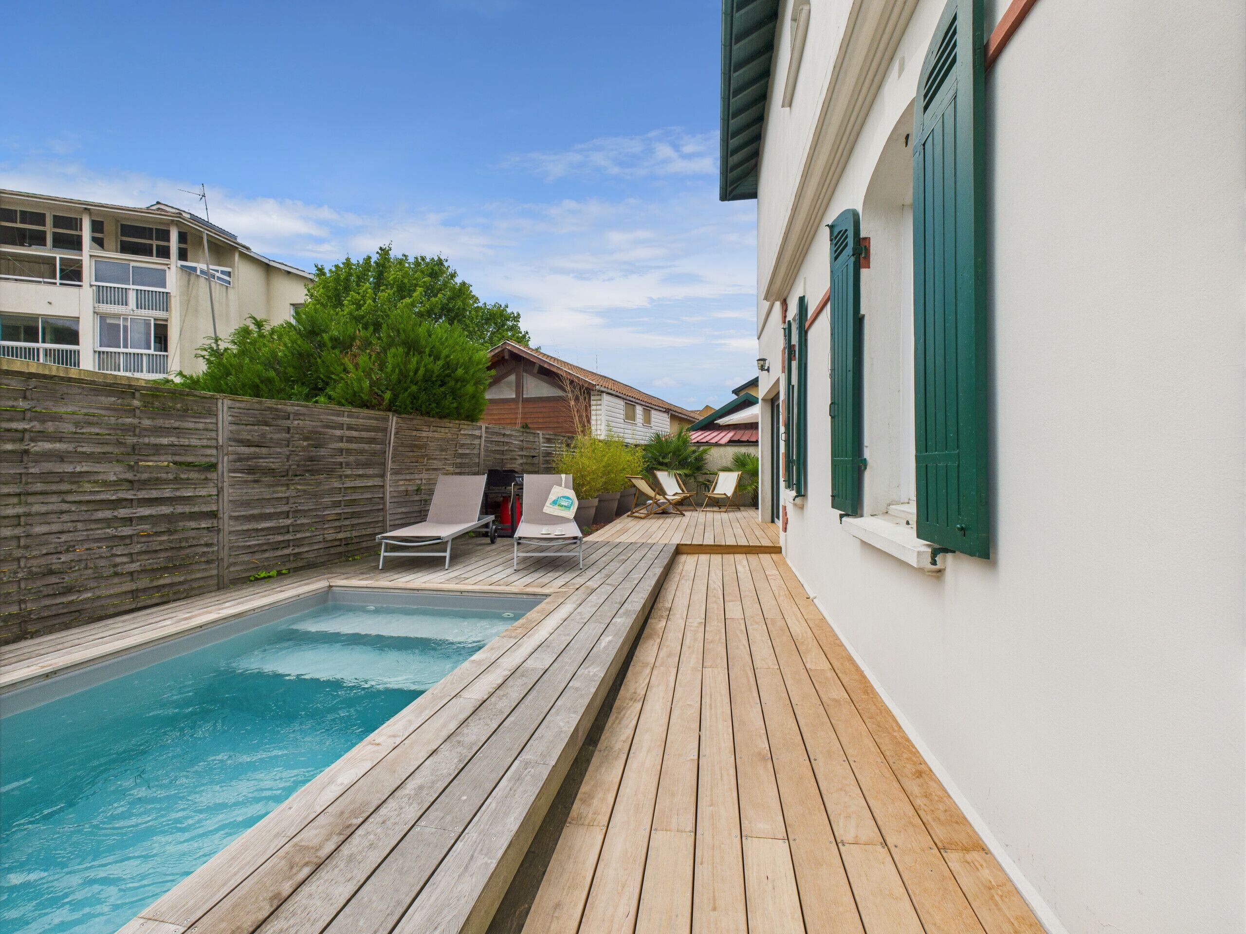 Une piscine avec une terrasse en bois, deux chaises longues et une clôture en bois.