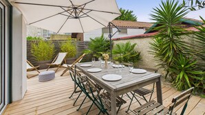 An outdoor patio with a wooden table set for dining, surrounded by green chairs and a large umbrella providing shade. - 300m from the beach, house for 7 with a pool (Lanton)