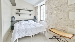 Une chambre avec un grand lit, un mur en pierre et une fenêtre.